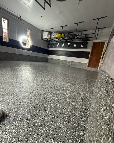 Garage with a grey flake epoxy floor, navy and white wall panels and overhead storage racks